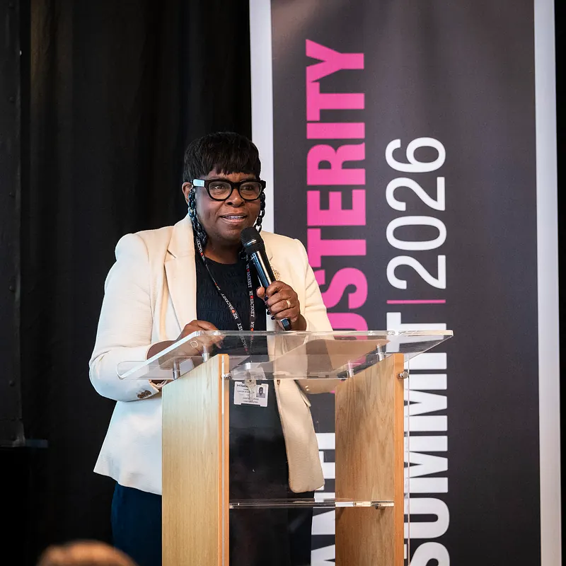 A speaker addresses the Anti-Austerity Summit from the lectern, in front of the summit banner