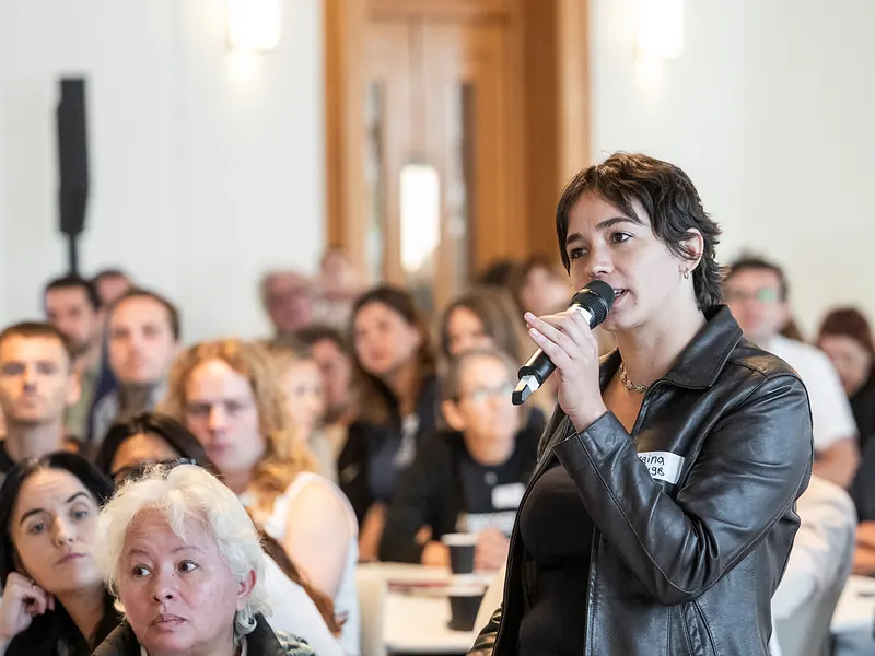A trade unionist speaks into a microphone from the floor while delegates at round tables turn to listen